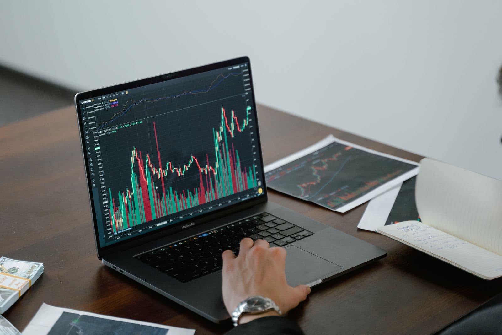 Person reviewing trading charts on a laptop beside notes and a tablet
